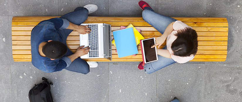 Two students with laptops sitting on a bench